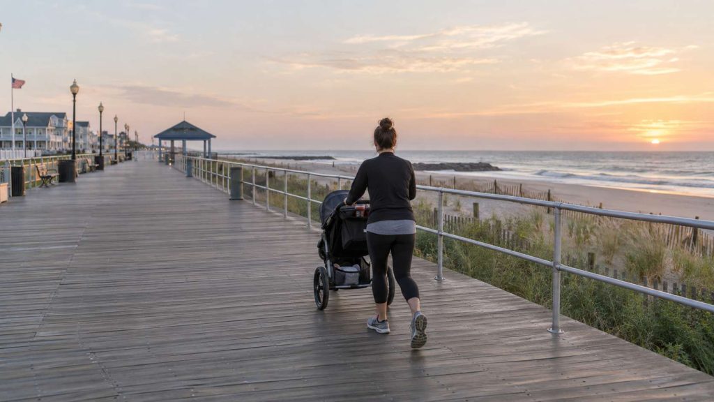 Parent pushing a jogging stroller along the Belmar, NJ boardwalk in morning light